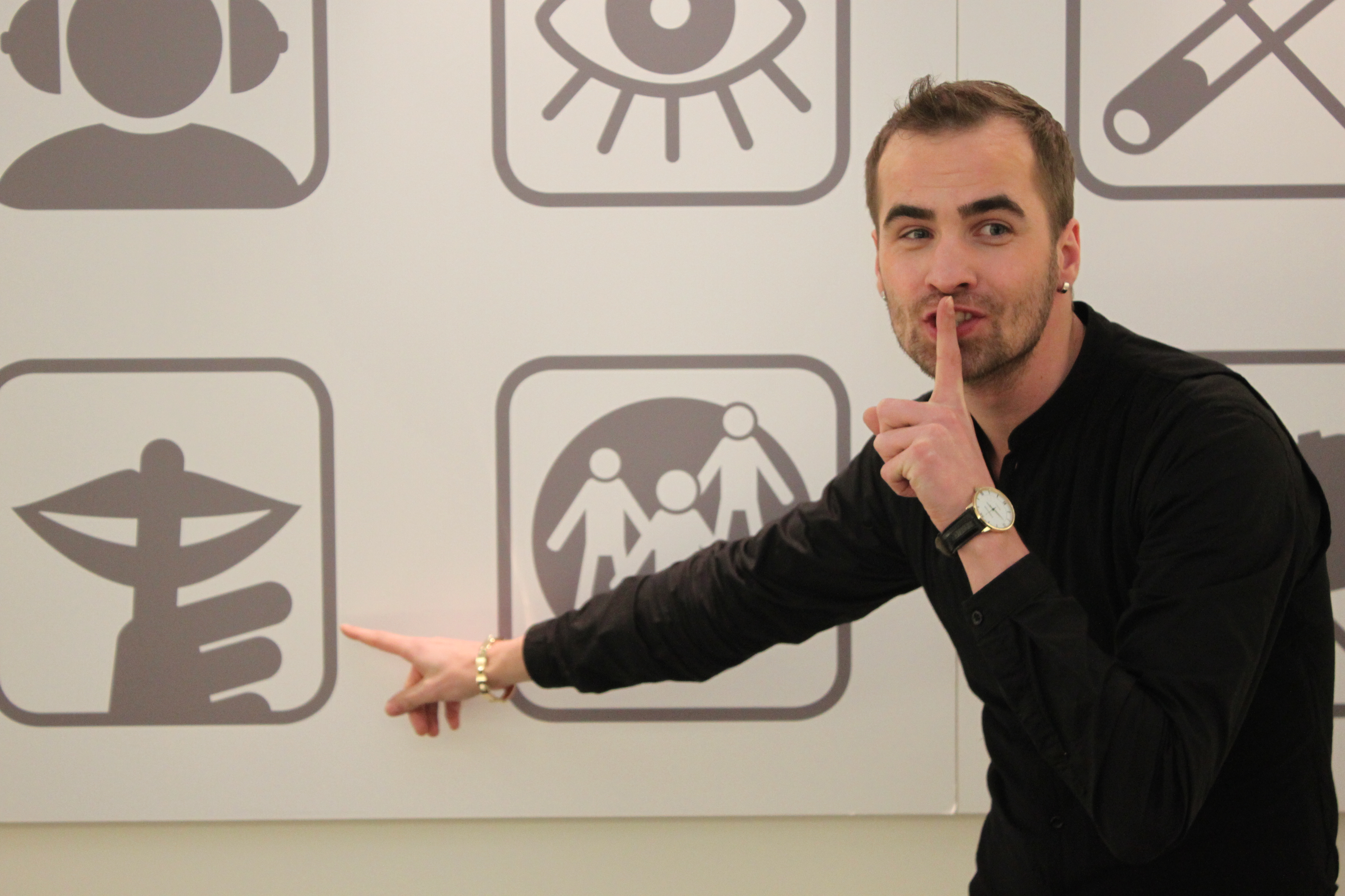 Guide Andres aus der Ausstellung Dialog im Stillen vor der Piktogramm Tafel