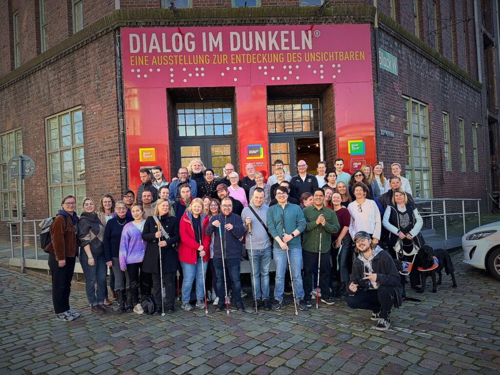 Ein Gruppenfoto zeigt die Mitarbeitenden des Dialoghauses Hamburg vor dem Haupteingang des Gebäudes.