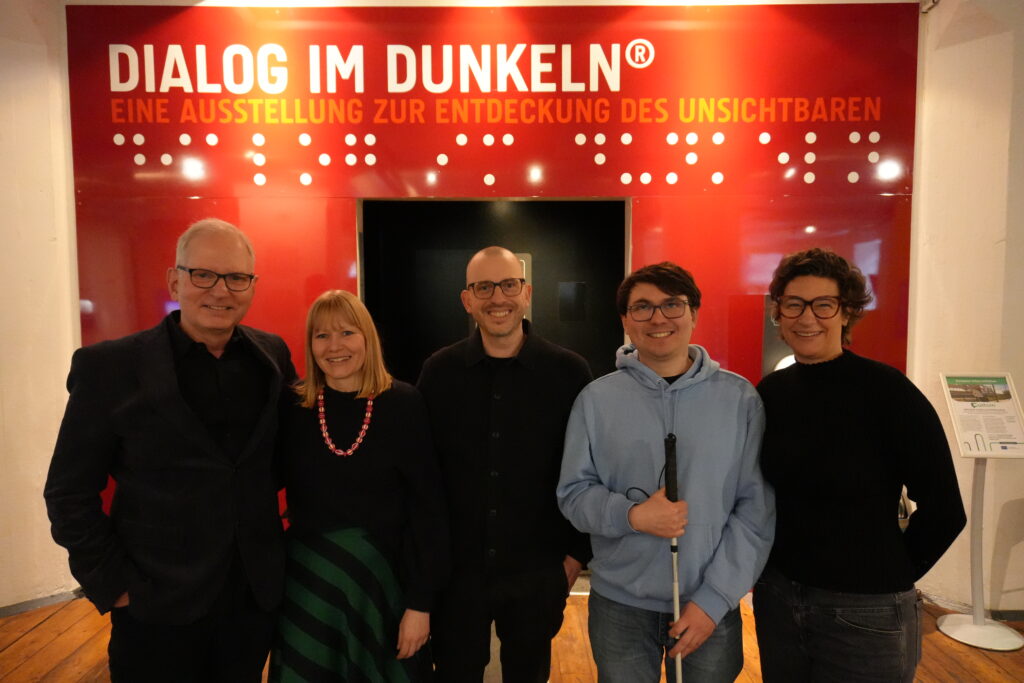 Mitarbeitende des Dialoghaus Hamburg stehen gemeinsam mit Jesper Götsch (Jazzunique) vor dem Eingang zu Dialog im Dunkeln.