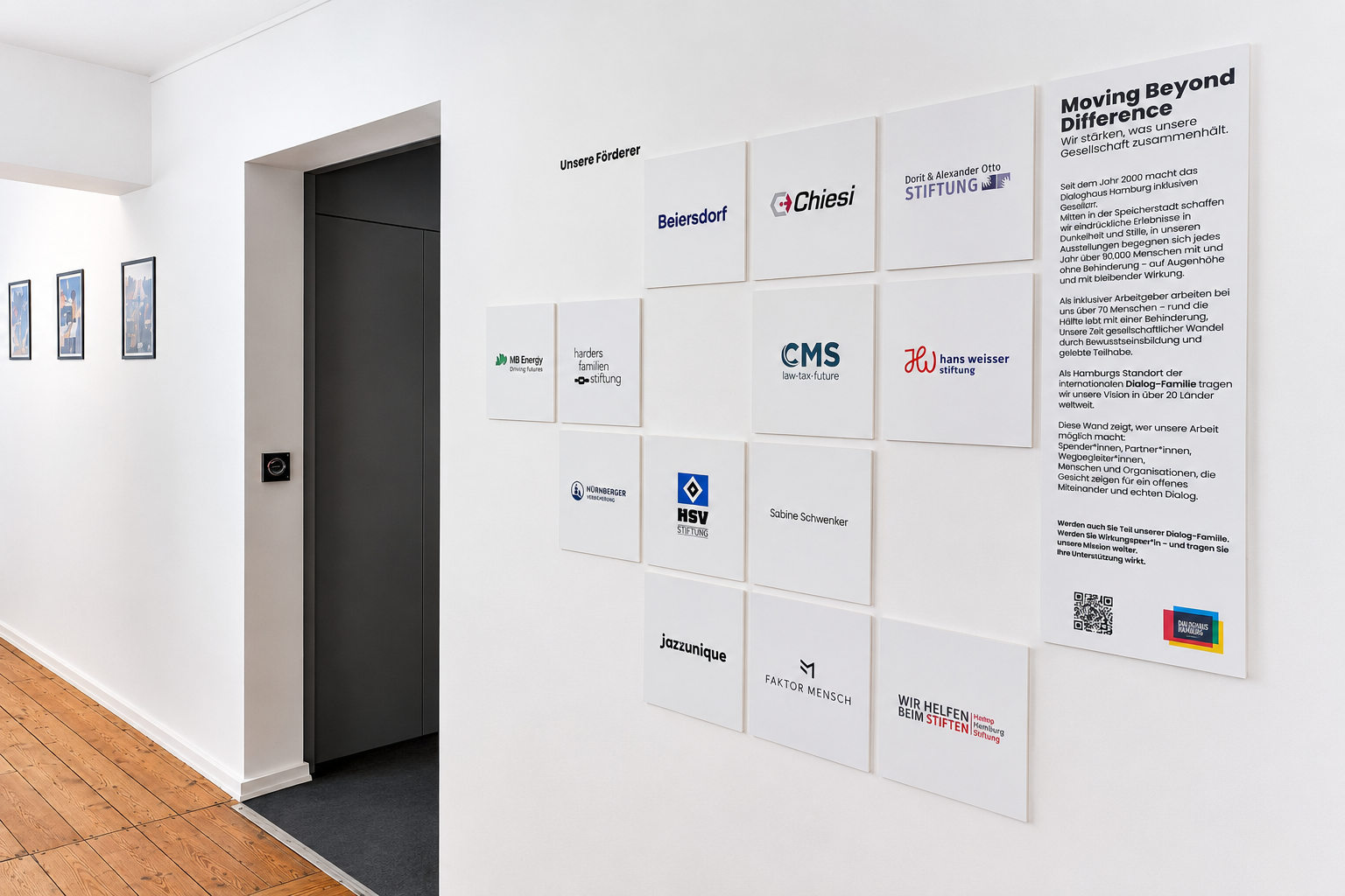 Heller Flur im Dialoghaus Hamburg mit einer Förderwand aus weißen Tafeln, Sponsor-Logos und einer Infotafel zur Mission „Moving Beyond Difference“.